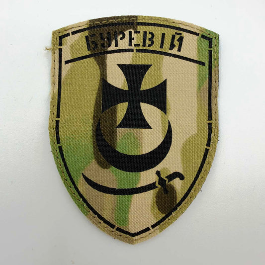 Shield-shaped camouflage patch with the Ukrainian word “БУРЕВІЙ” across the top, a black flared cross above an upward-facing crescent, and a curved sabre below.