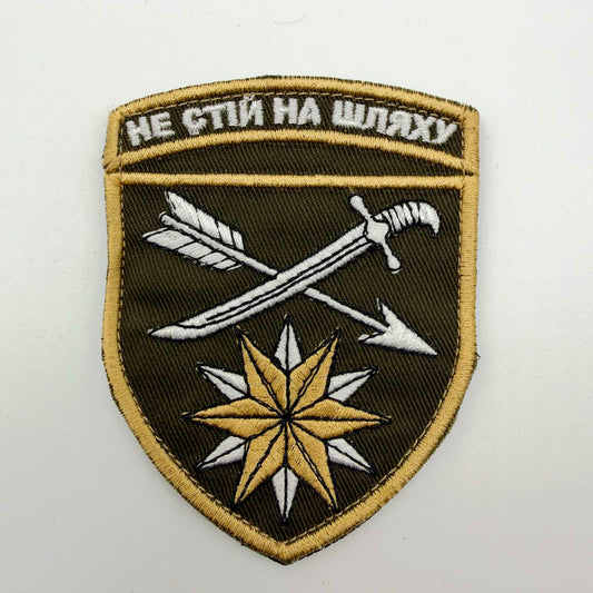 Dark olive shield-shaped embroidered patch with gold-coloured edging, a white crossed sabre and arrow, overlapping gold and white six-pointed stars, and the Ukrainian motto “НЕ СТІЙ НА ШЛЯХУ” across the top.