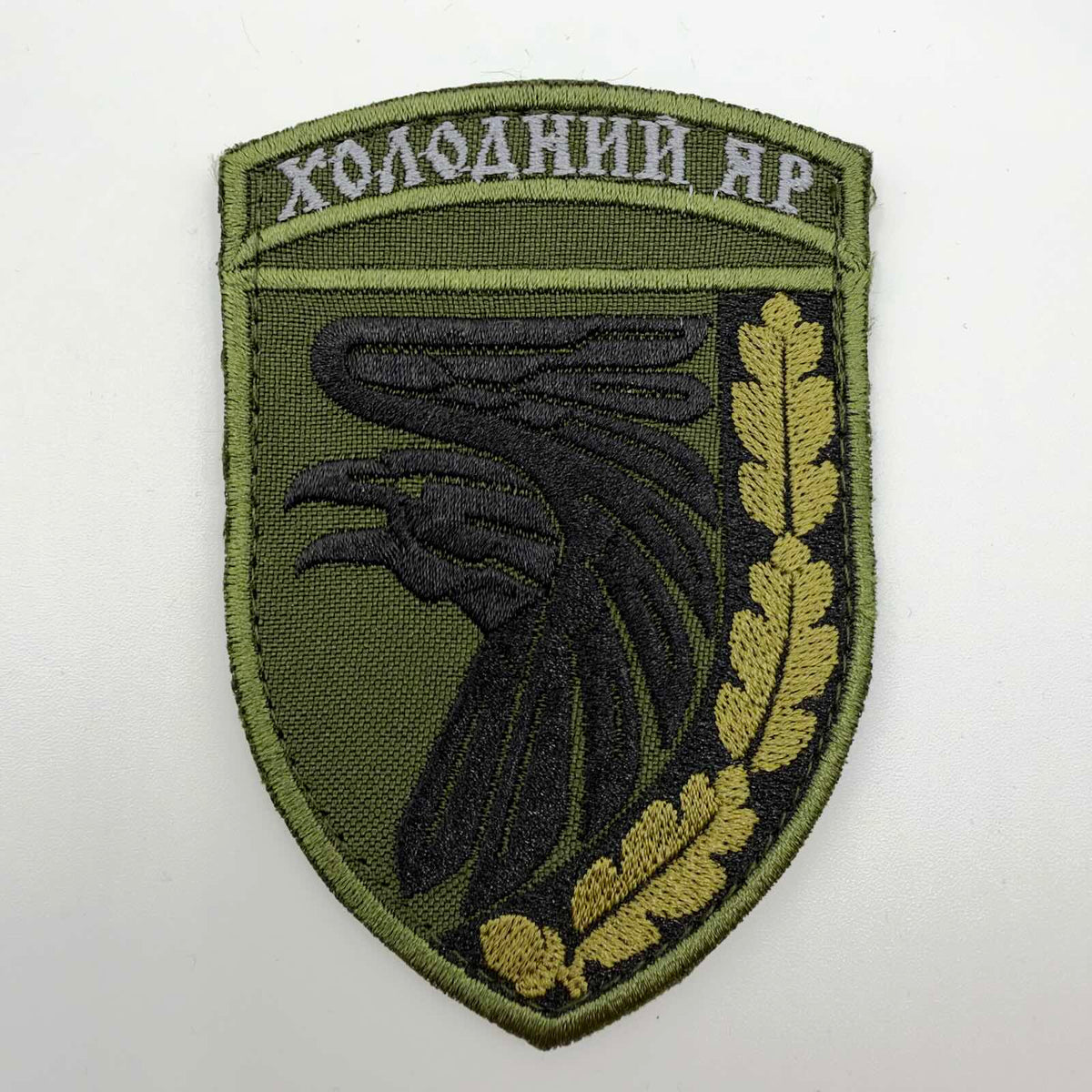 Olive-green shield-shaped embroidered patch with a black raven, golden-olive oak leaves and acorns, and the Ukrainian inscription “ХОЛОДНИЙ ЯР” across the top.