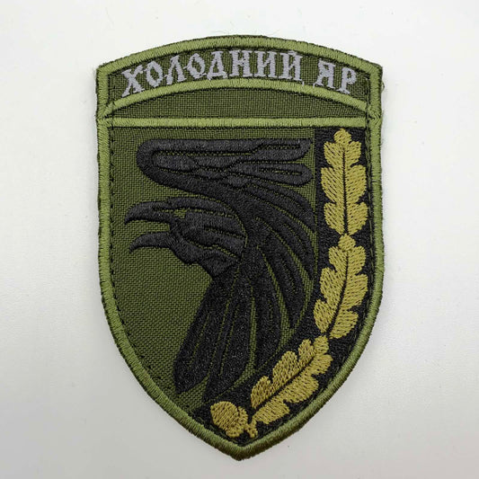 Olive-green shield-shaped embroidered patch with a black raven, golden-olive oak leaves and acorns, and the Ukrainian inscription “ХОЛОДНИЙ ЯР” across the top.
