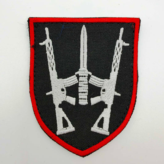 Black shield-shaped embroidered patch with a red border and two white rifles flanking a central upright blade, arranged in a stylised trident.