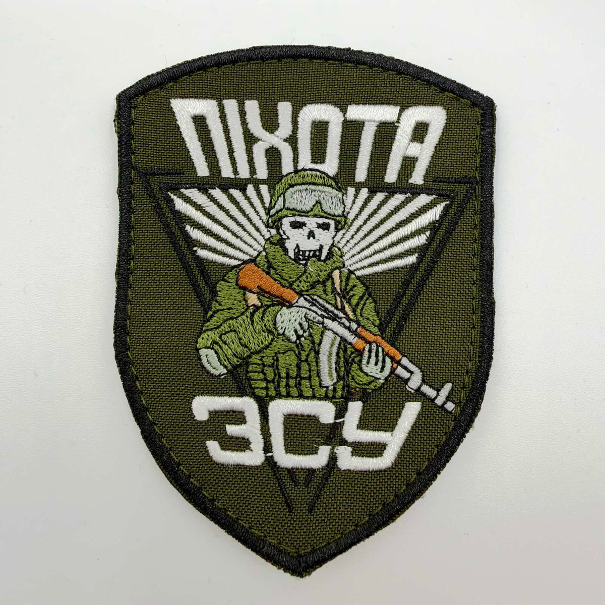 Olive-green shield-shaped embroidered morale patch with Ukrainian text reading “Infantry” and “Armed Forces of Ukraine”, featuring a skull-faced soldier in a helmet and goggles holding a rifle against white radiating lines.