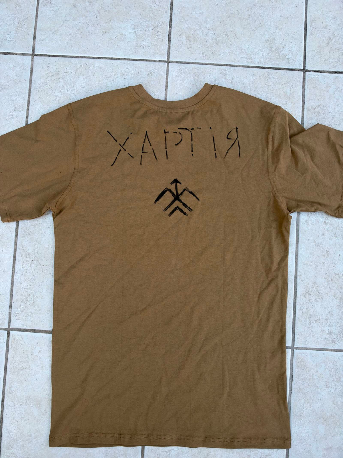 Back of a khaki military T-shirt with the Ukrainian word “ХАРТІЯ” and a black hand-drawn Khartiia emblem beneath it.