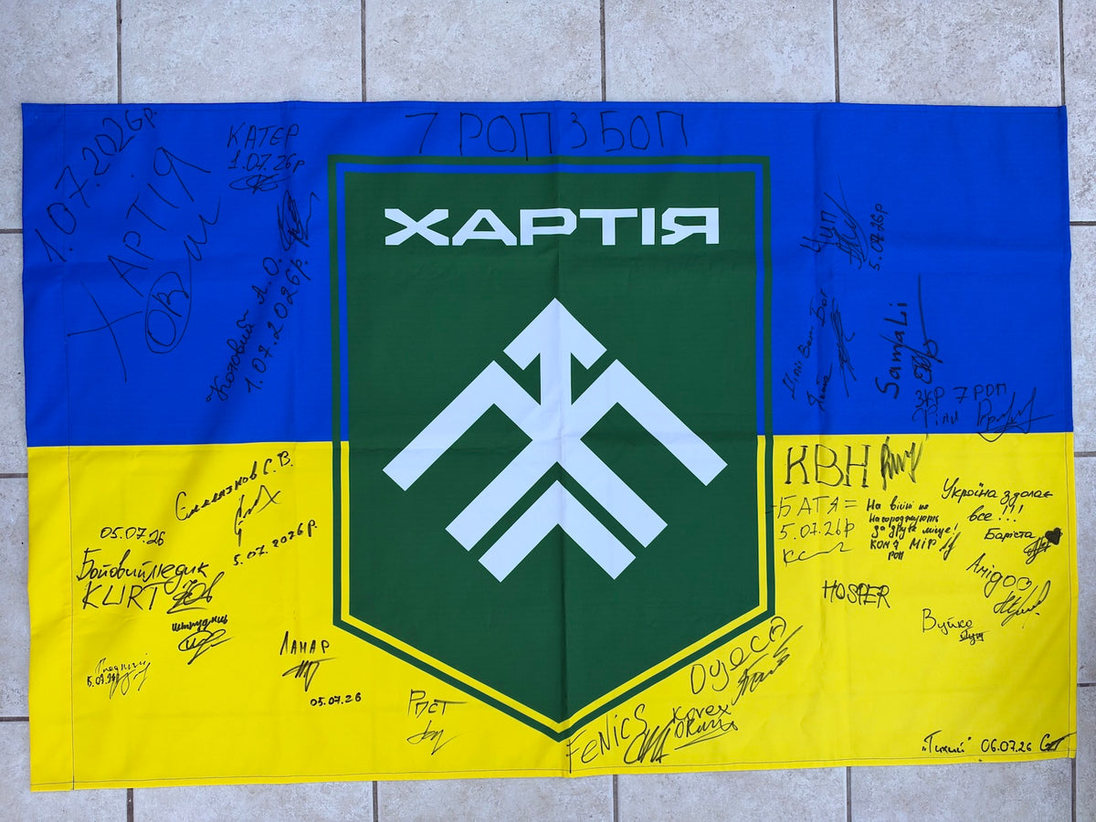 Blue-and-yellow Ukrainian flag with a large green Khartiia shield and white emblem, surrounded by handwritten signatures, messages and July 2026 dates.