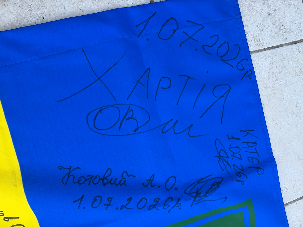 Close-up of the flag’s upper-left blue section showing handwritten Khartiia lettering, names, signatures and dates of 1 July 2026.