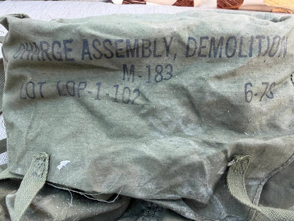 Close-up of the bag’s faded black M-183 demolition assembly markings, dusty fabric and frayed flap edge.