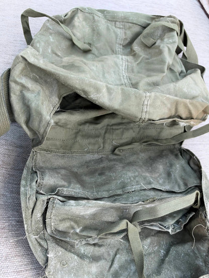 Open military bag showing dusty olive-green fabric, webbing ties, loose threads and separated seams.