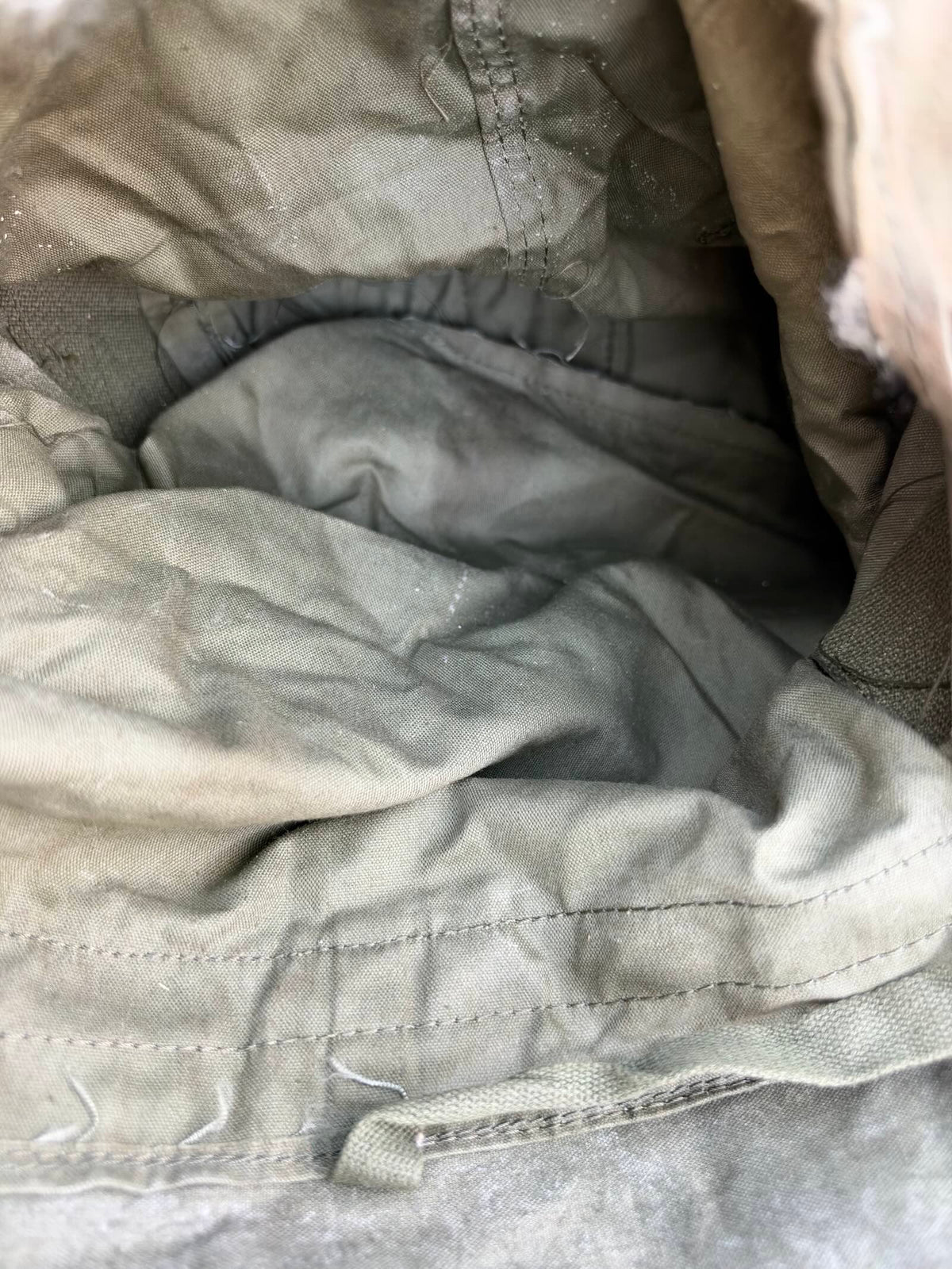 Close-up inside the worn military bag, showing creased fabric, stitching, dust and loose threads.