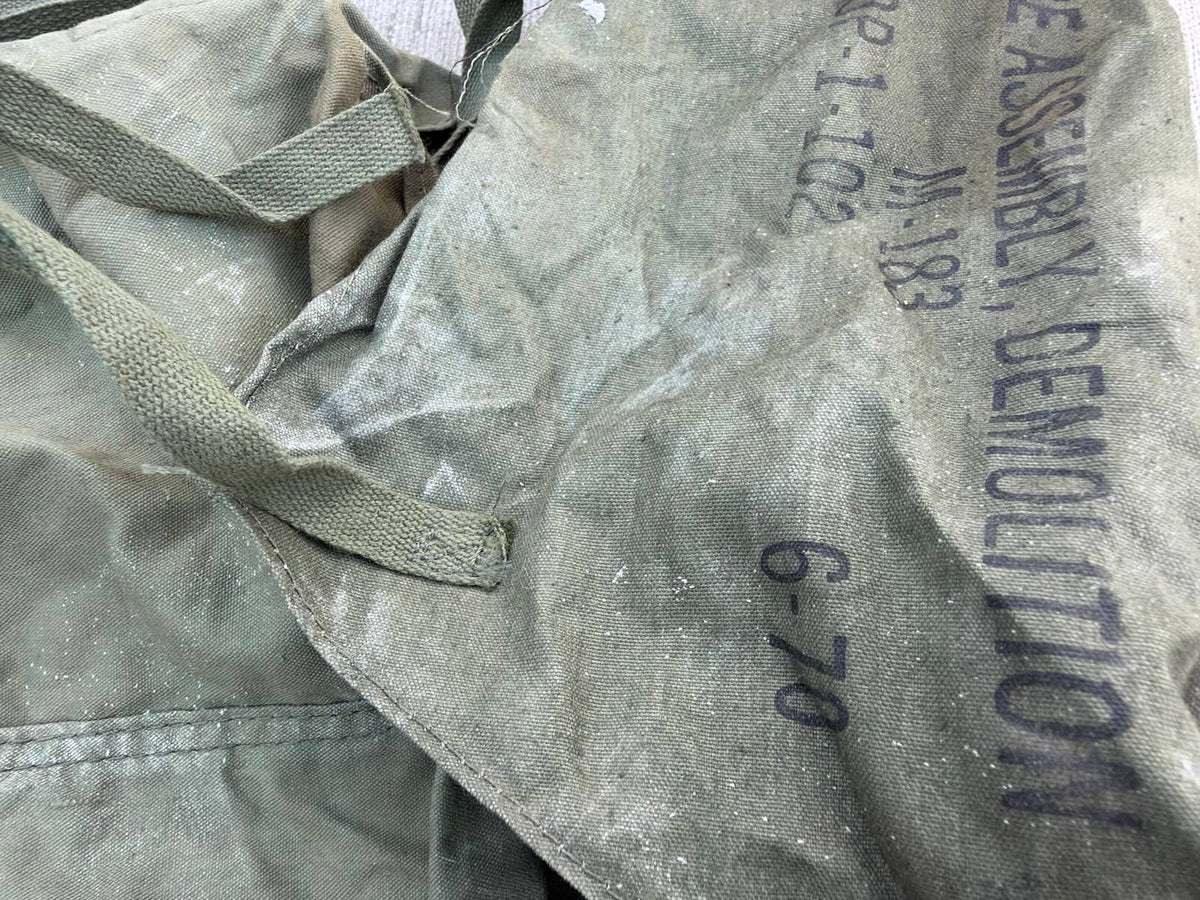 Detail of the bag’s marked flap, showing “M-183”, “6-78”, webbing ties and extensive surface dust.