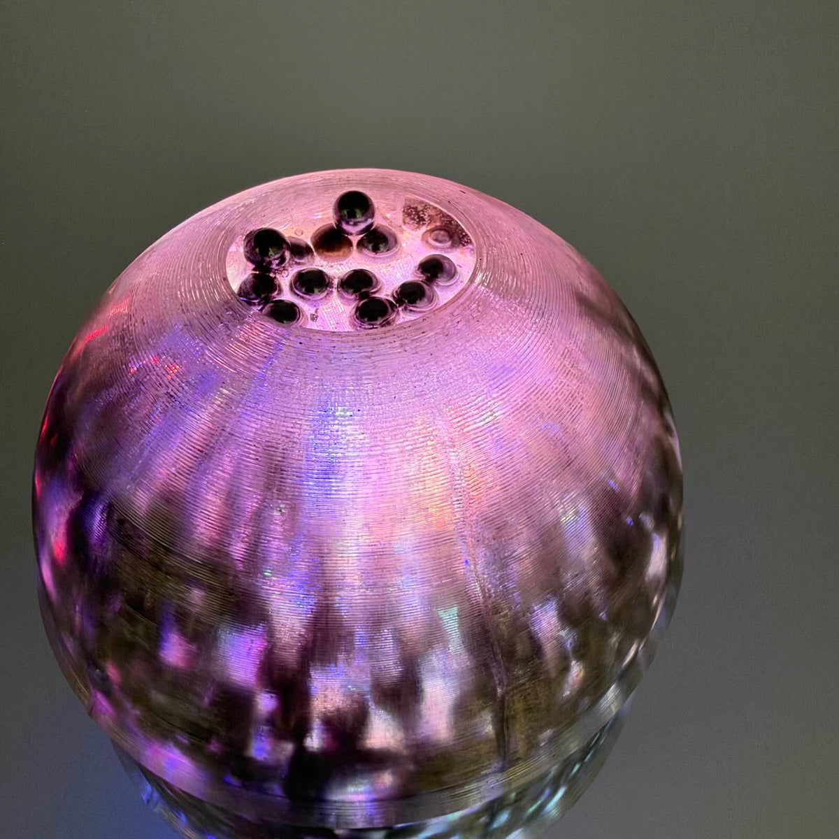Close-up of a translucent 3D-printed munition-shaped light glowing pink and purple, with metal ball bearings visible in resin.