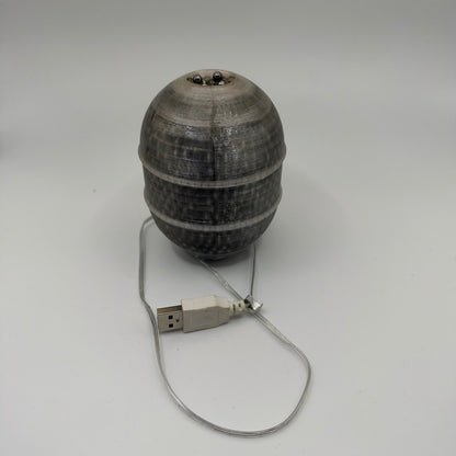 Unlit munition-shaped resin-filled LED lamp with a ribbed translucent body, visible ball bearings and a USB-A power cable.