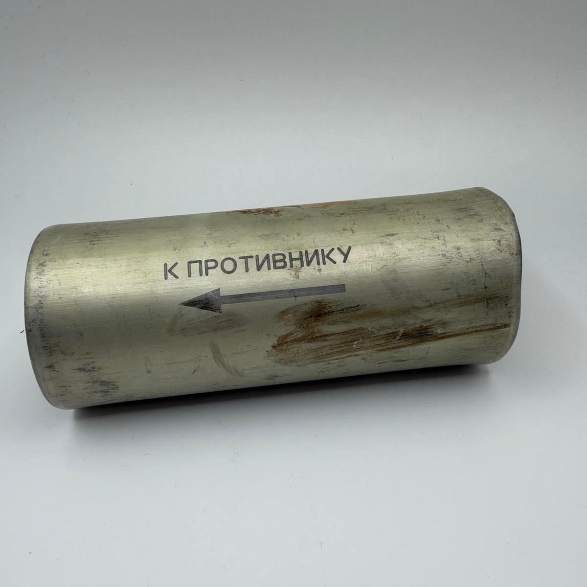 Worn metal cylinder marked in Russian “Towards the enemy”, with a black arrow pointing left.