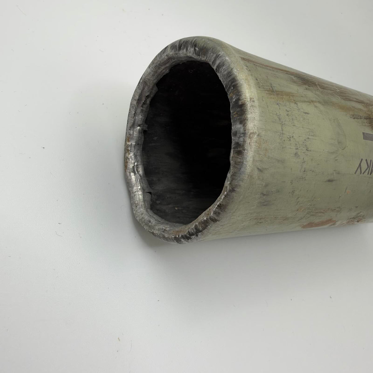 Close-up of the cylinder’s opposite opening, showing a rough inward-curved metal edge and dark interior.