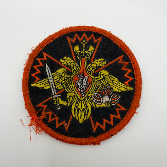 IMG_0602.jpeg: Worn circular Russian patch with a gold double-headed eagle, sword and flaming grenade over an orange carnation outline, with a frayed orange border.