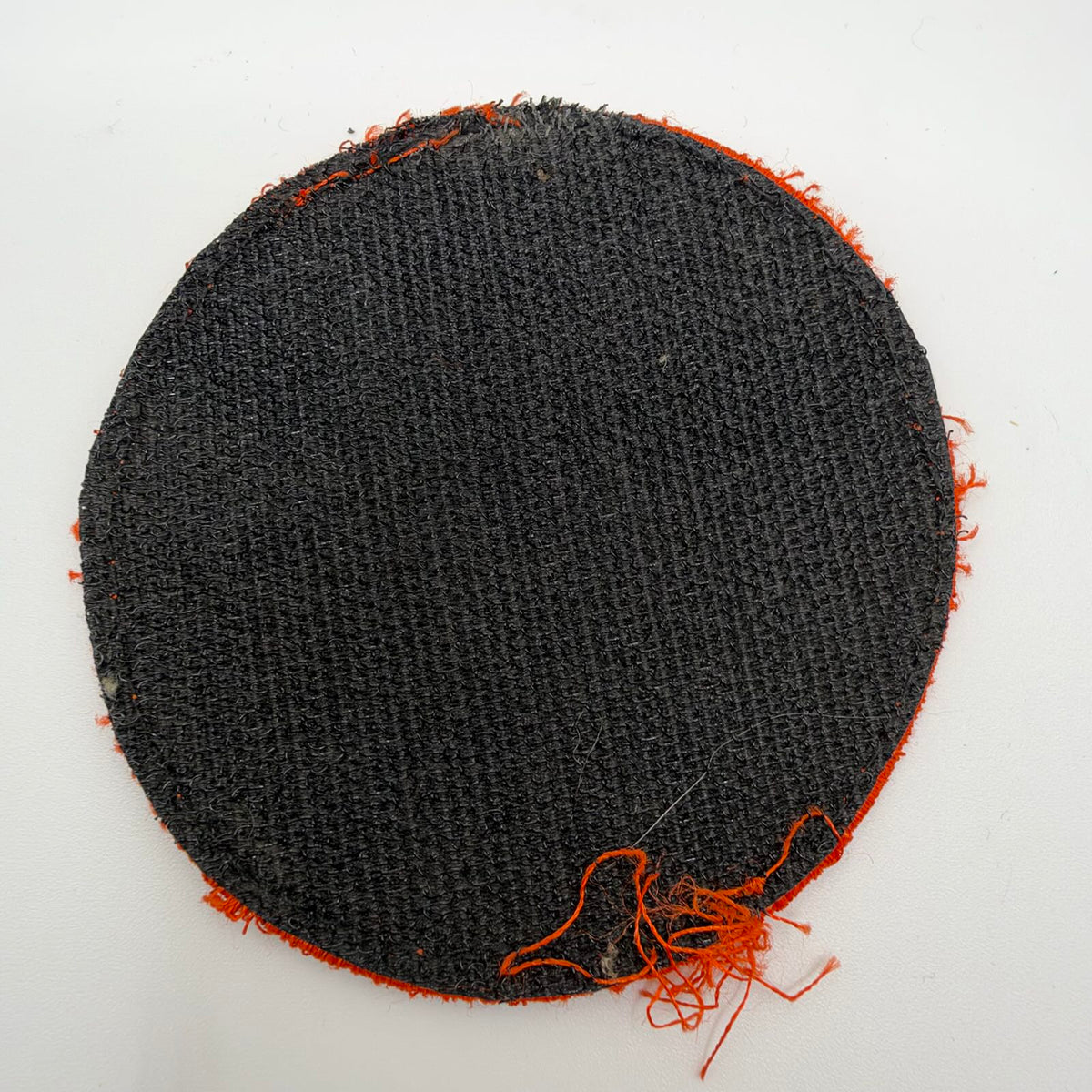 - Reverse of the circular patch showing black hook-and-loop backing, worn stitching and loose orange threads around the edge.