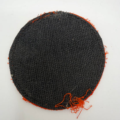 - Reverse of the circular patch showing black hook-and-loop backing, worn stitching and loose orange threads around the edge.