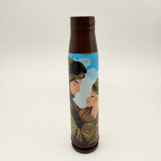 Decorated shell casing with a brown neck and base, showing a couple in military clothing leaning together, eyes closed, against a blue sky with white clouds.