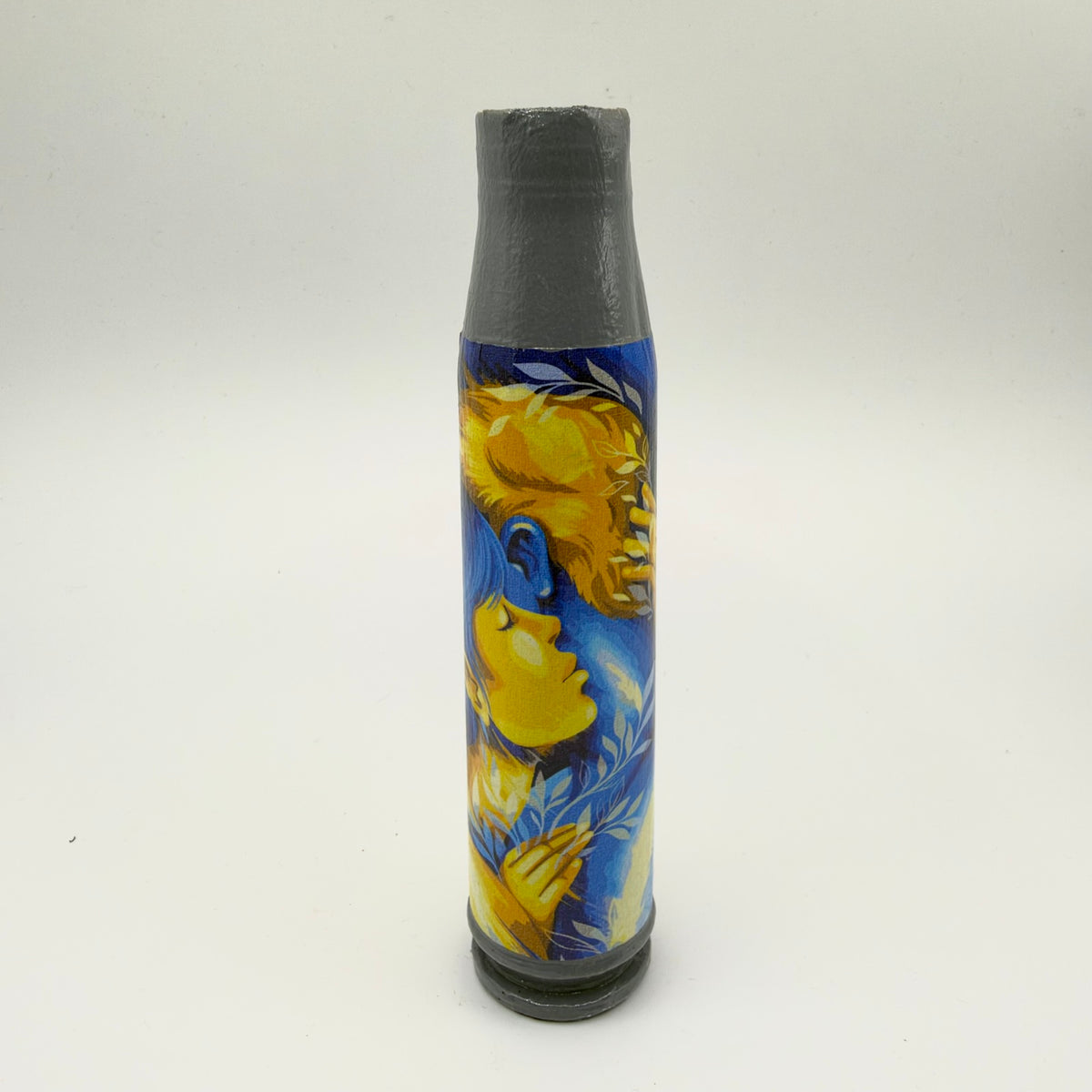 Decorated shell casing with a grey neck and base, showing two people embracing in blue and golden-yellow tones, surrounded by pale leafy branches.