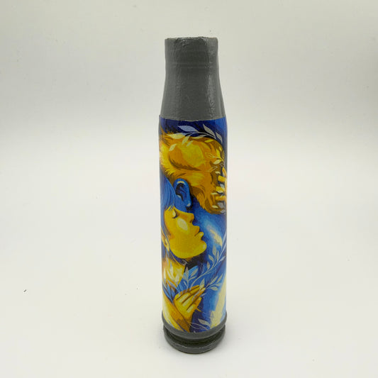 Decorated shell casing with a grey neck and base, showing two people embracing in blue and golden-yellow tones, surrounded by pale leafy branches.