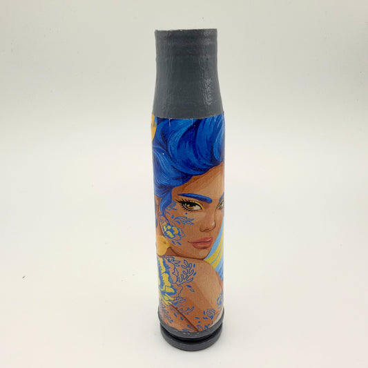 Decorated shell casing with a grey neck and base, showing a woman with swept-up blue hair and blue and yellow floral patterns across her cheek and shoulder.