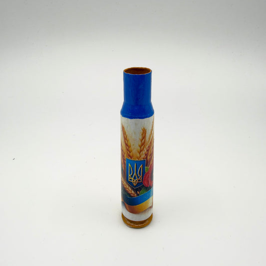 Decorated casing with a blue neck and golden-brown base, showing a gold Ukrainian trident on a blue shield among wheat, a red poppy and a blue and yellow ribbon.