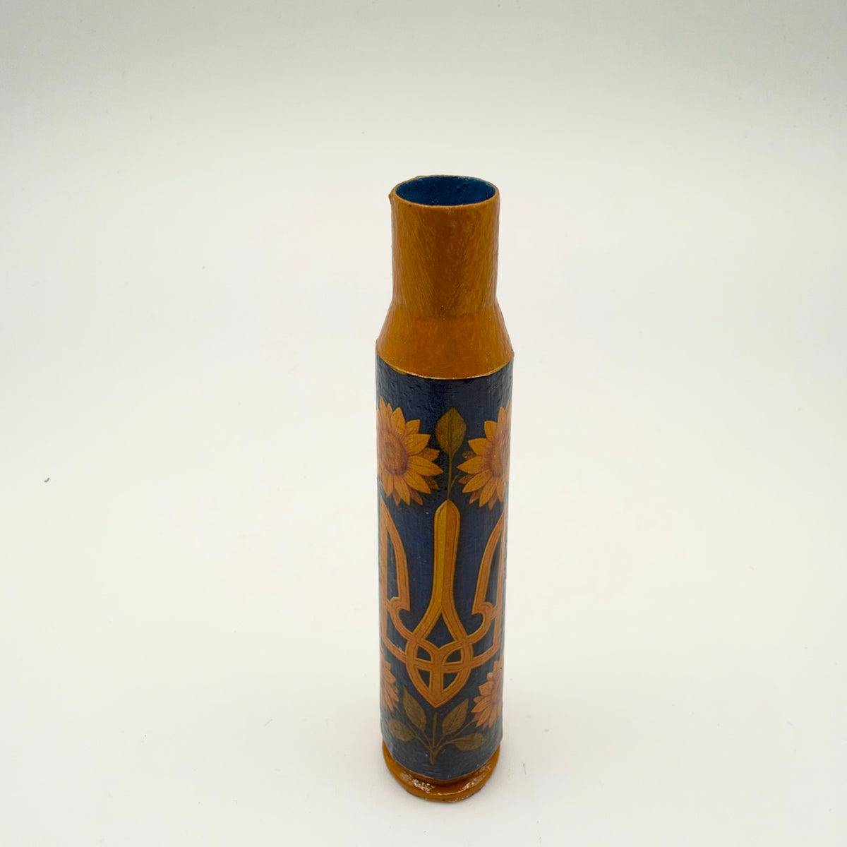 Decorated casing with an ochre-gold neck and base, featuring a large golden-orange Ukrainian trident surrounded by sunflowers and leafy stems on a slate-blue background.