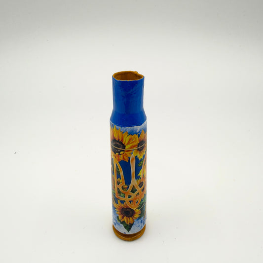 Decorated casing with a blue neck and golden-yellow base, featuring a golden Ukrainian trident surrounded by yellow sunflowers and green leaves on a blue and white background.