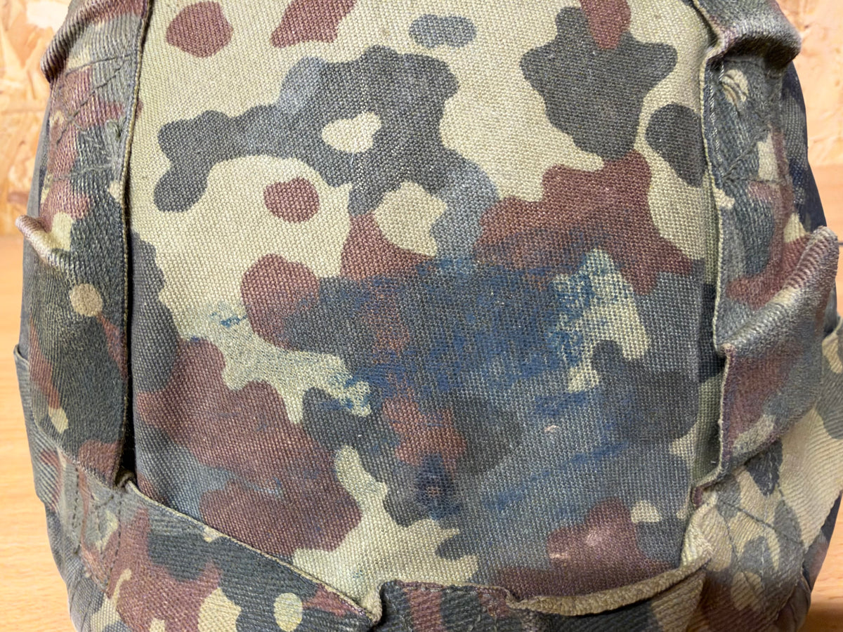 Close-up of the faded Flecktarn helmet cover, showing dirt, staining, abrasions and wear from service.
