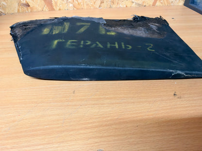 Low side view of the crash-damaged Geran-2 lower tail stabiliser, showing its curved profile, black outer skin and yellow identification markings.