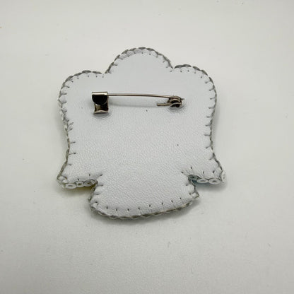 Reverse of the angel-shaped brooch showing a white textured backing with visible stitching around the outline. A horizontal silver-coloured brooch pin and clasp sit across the upper section, with translucent edging beads visible around the perimeter.
