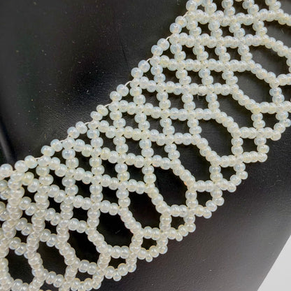 Close-up of the necklace’s ivory-coloured beads against a black display bust, showing their pearly sheen and intricate lace-like construction. Linked geometric openings lead into elongated beaded loops with small scallops along the outer edge.
