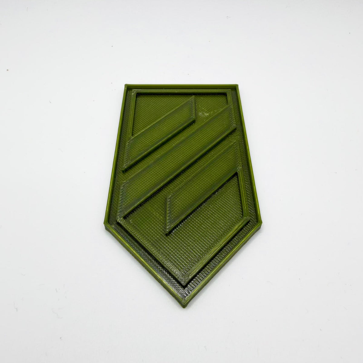 Olive-green 3D-printed replica of the Azov emblem on a shield-shaped base, with a raised angular symbol, recessed background and double border. Fine print lines are visible across the surface. Photographed on a white background.