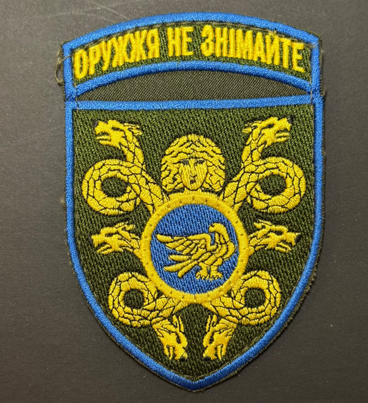 Embroidered patch with green background, yellow text, and blue border on a dark background