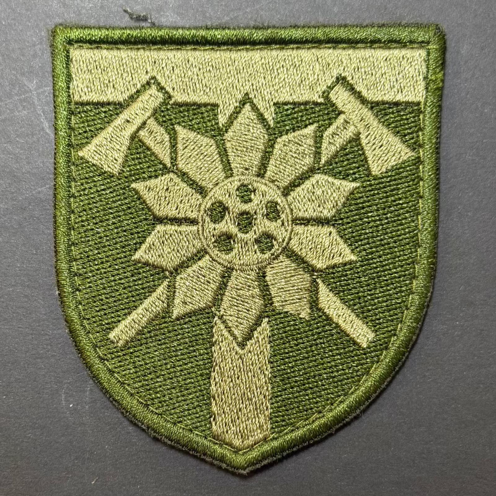 Green embroidered patch with a central design on a gray background