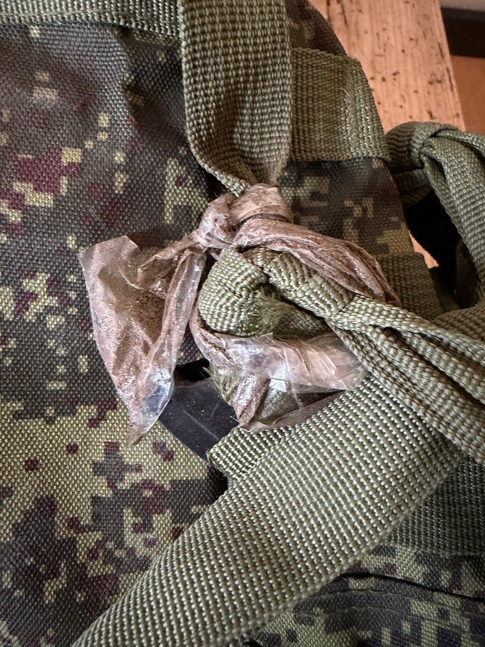 Close-up of a camouflage bag with a knot and plastic wrap on a wooden surface