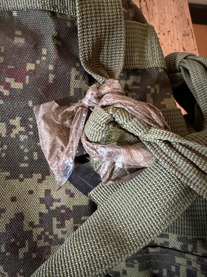 Close-up of a camouflage bag with a knot and plastic wrap on a wooden surface