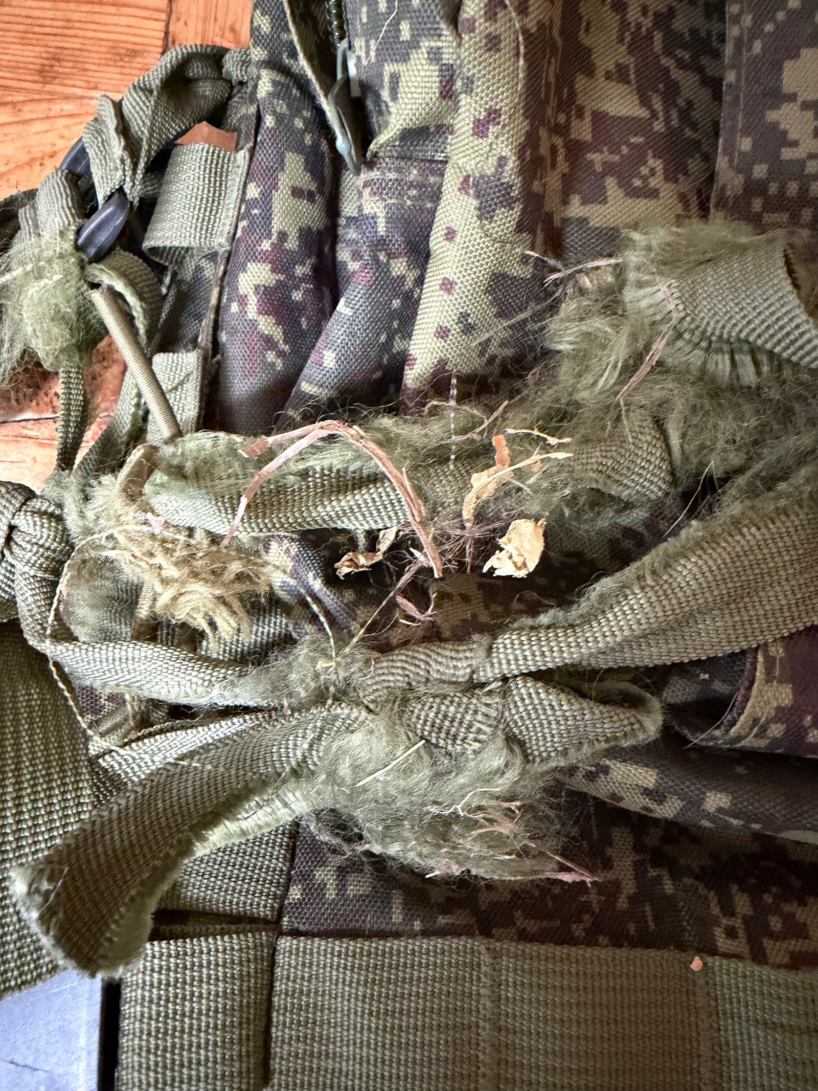 Close-up of a camouflage-patterned bag with a clear plastic cover on a wooden surface.