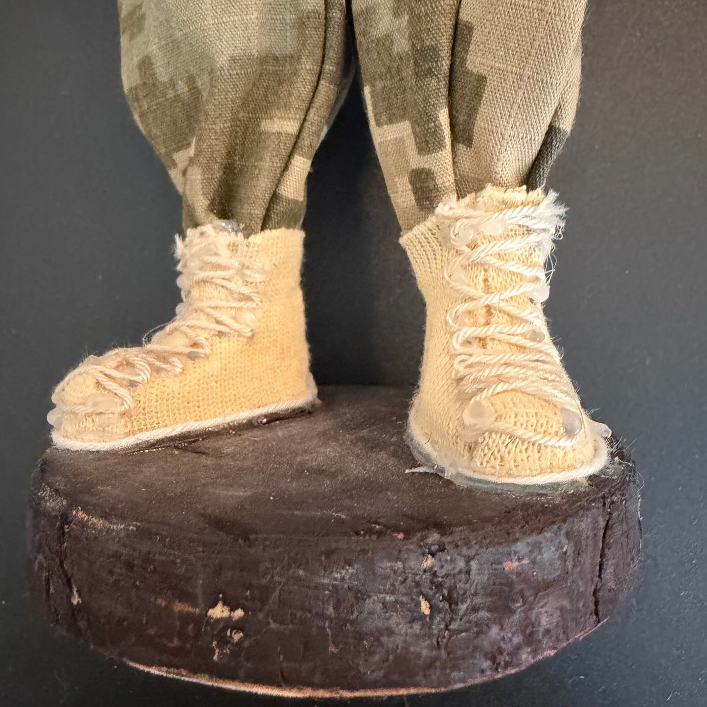 Close-up of a figure's feet wearing beige boots and camouflage pants on a dark background