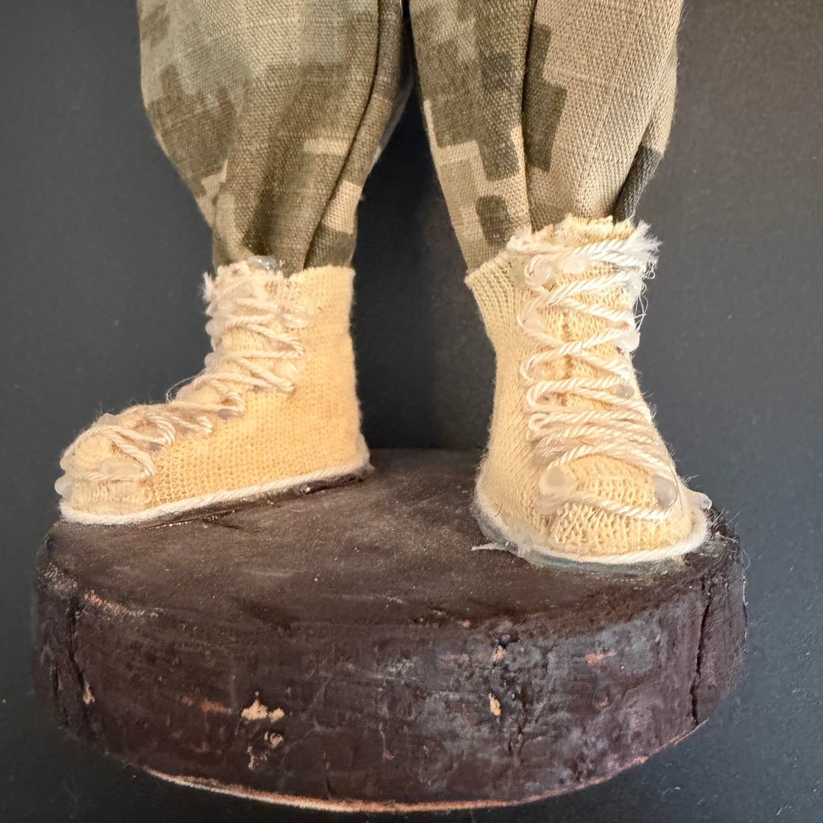 Close-up of a figure's feet wearing beige boots and camouflage pants on a dark background