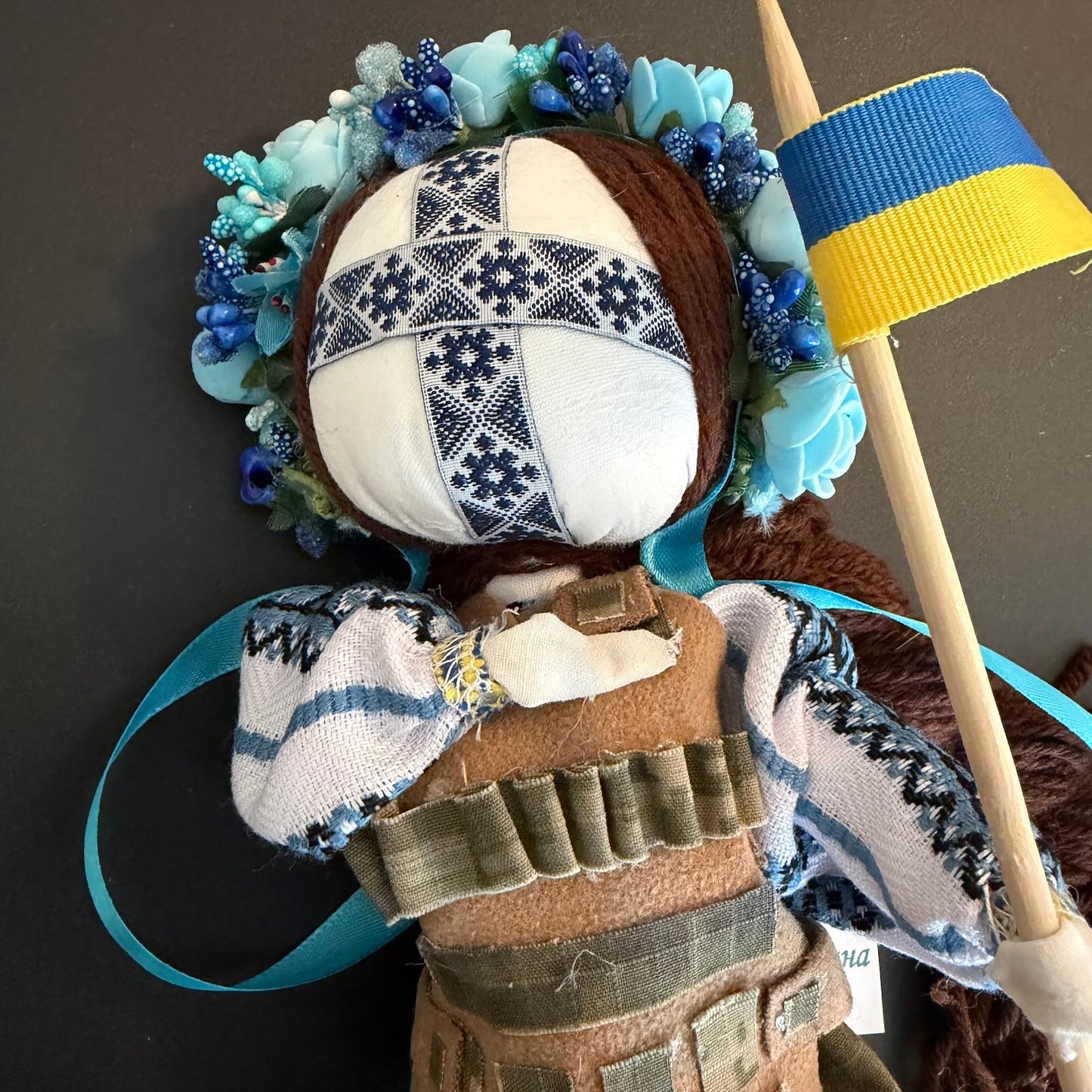 Doll with floral headpiece, bandaged head, and holding a flag against a dark background