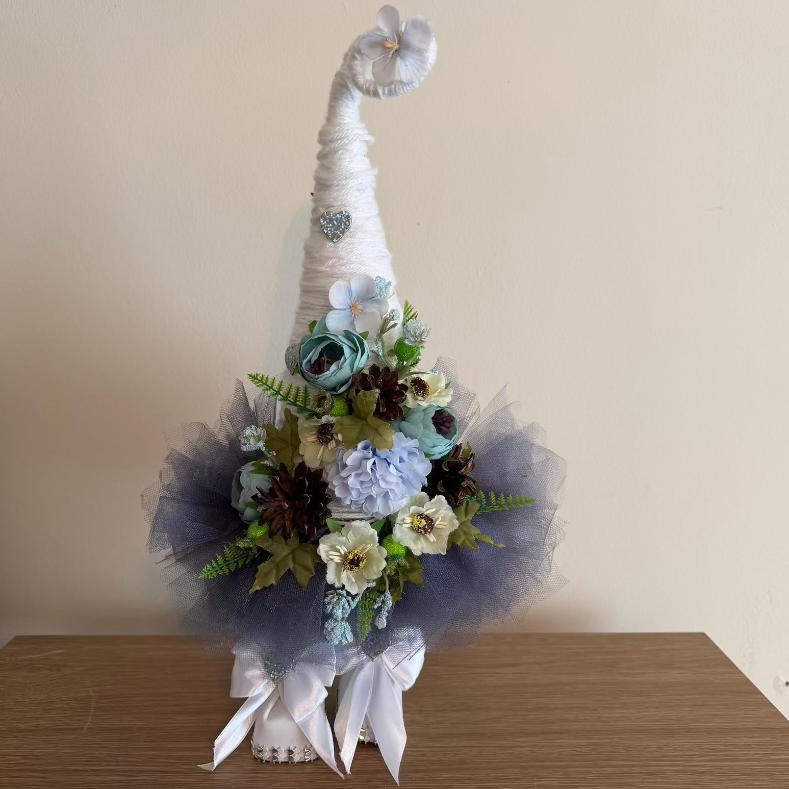 Decorative floral arrangement in a cone-shaped vase on a wooden surface with a beige background