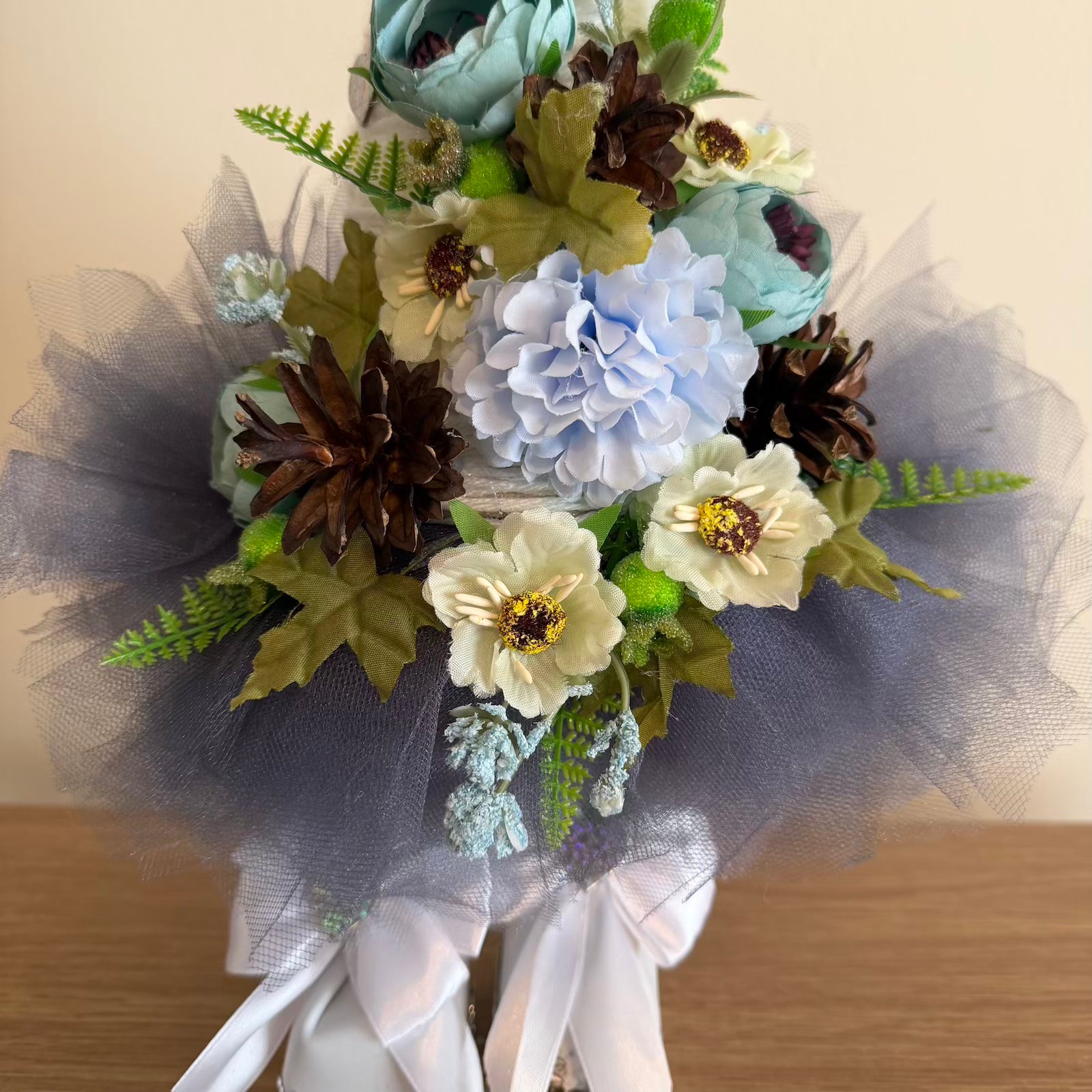 Bouquet of artificial flowers with tulle and ribbons on a wooden surface