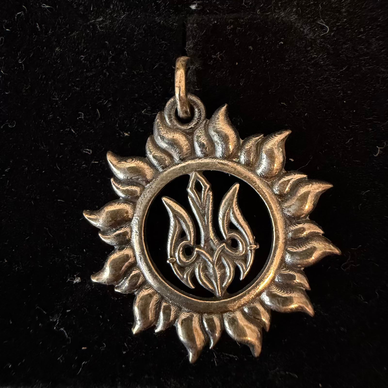 Silver pendant with a sun design on a black background