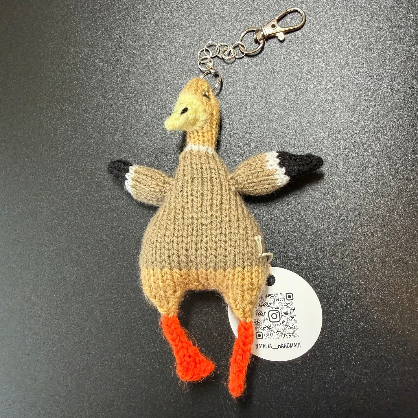Knitted Goose keychain with a tag on a dark background