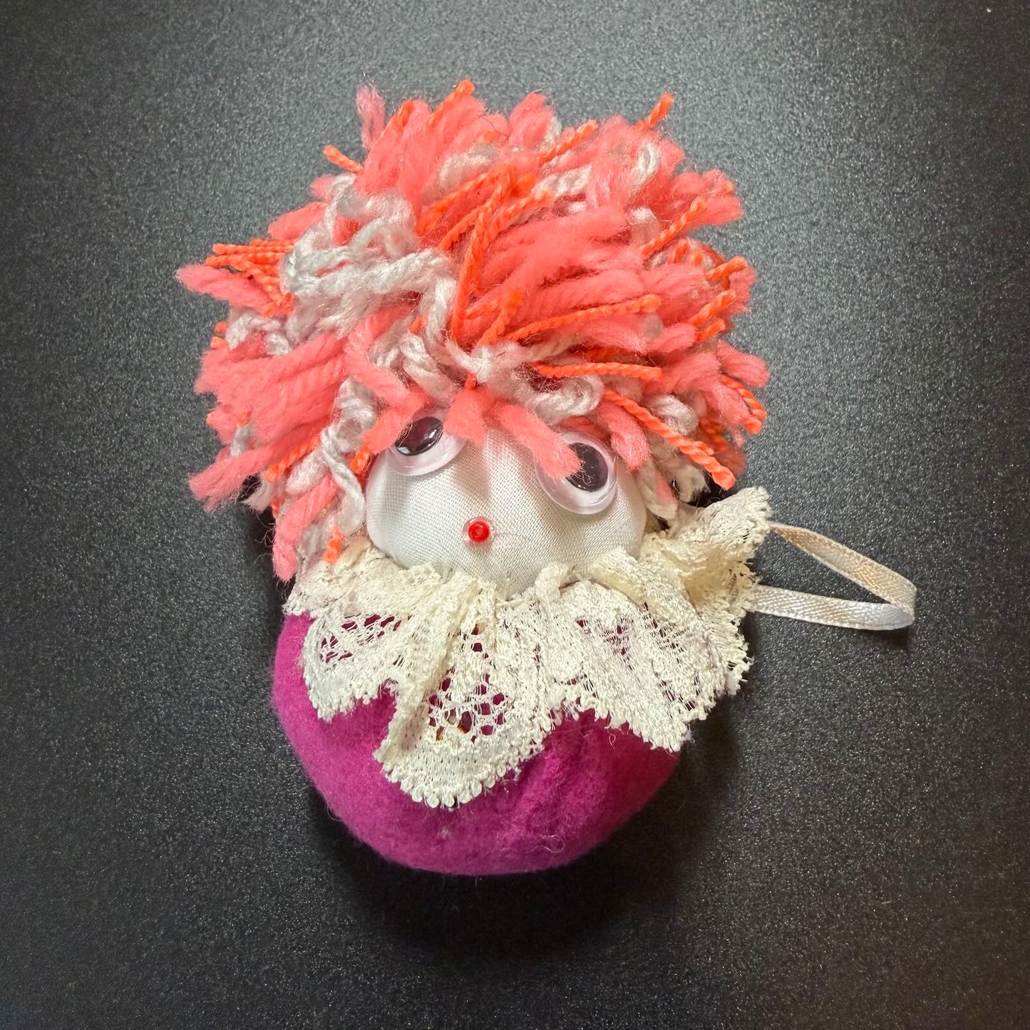 Decorative ornament with pink hair and lace detail on a dark background