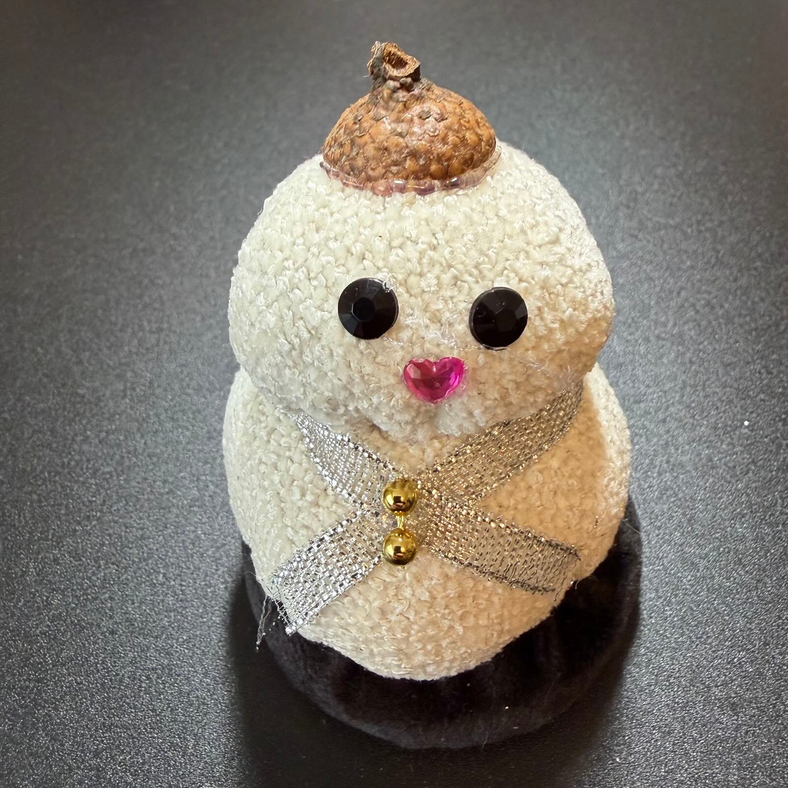 Decorative snowman figure with acorn hat on a dark surface
