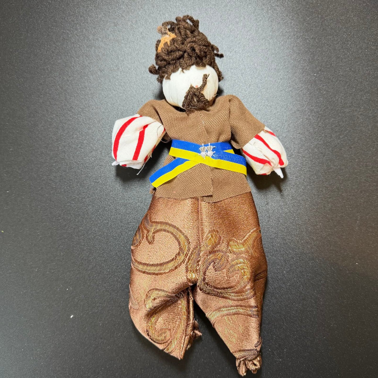 Puppet with a brown outfit and colorful belt on a gray background