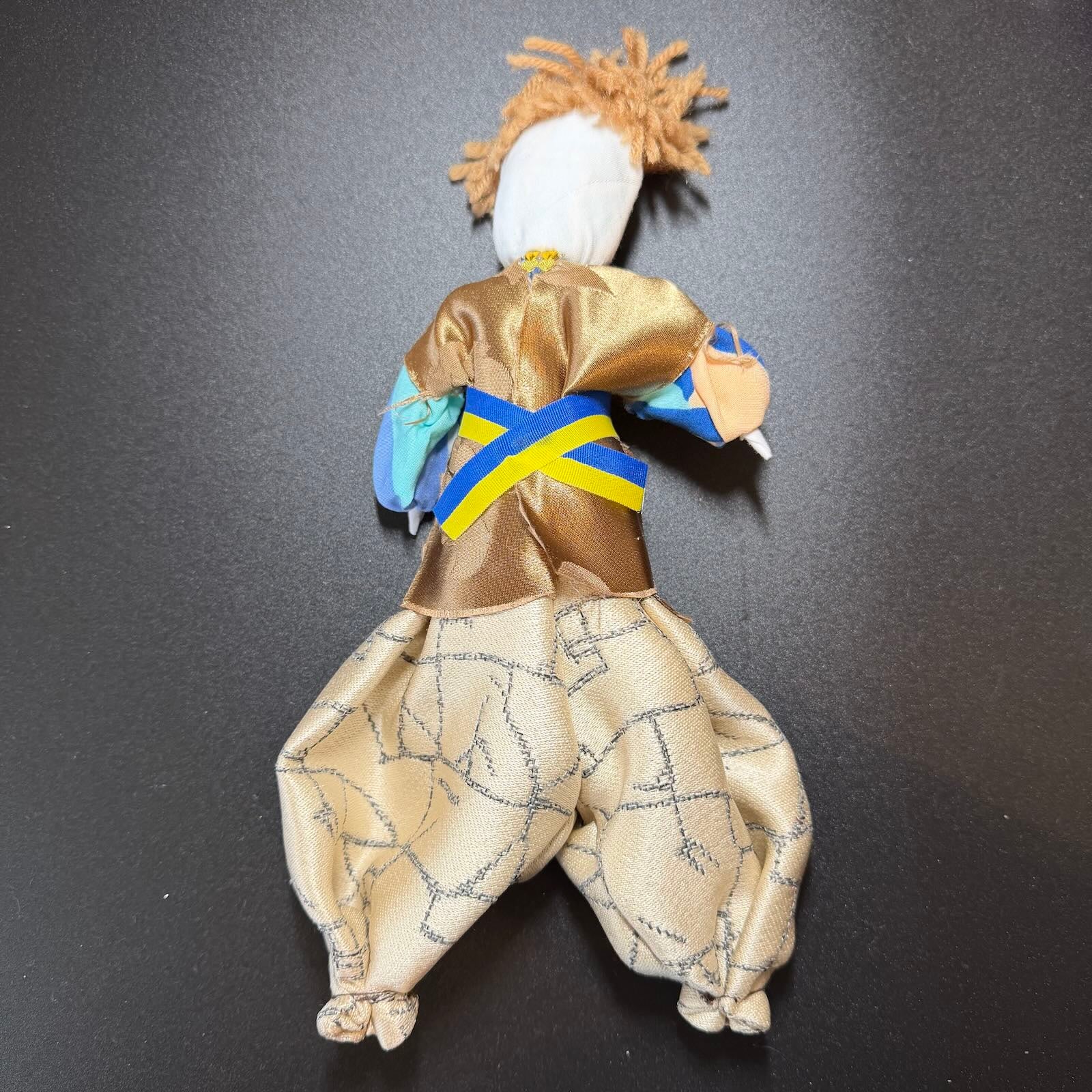 Textile figure with a gold outfit and blue sash on a black background