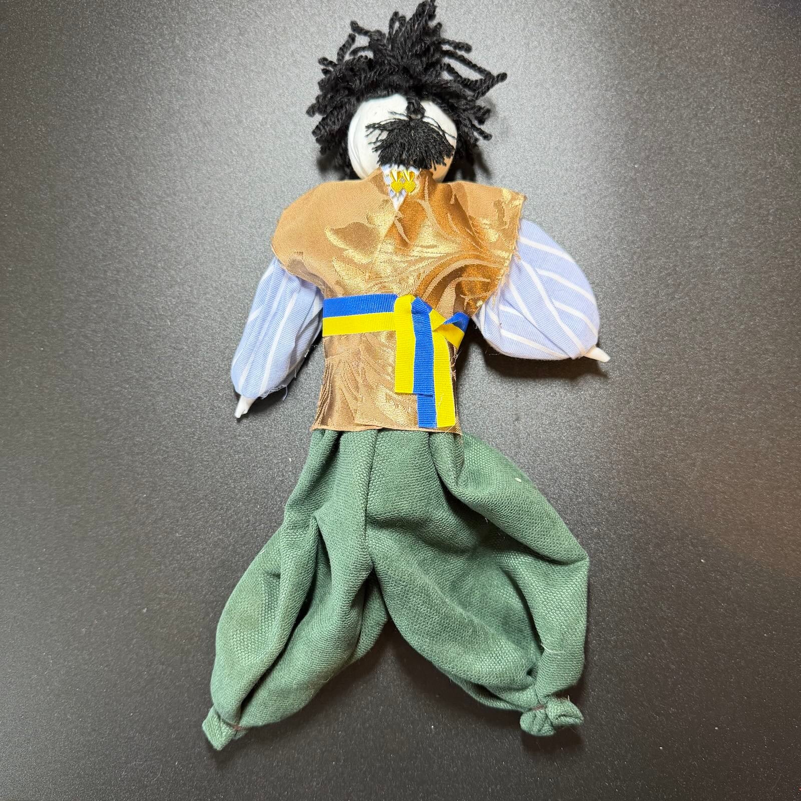 Handmade doll with green pants and a brown top on a gray background