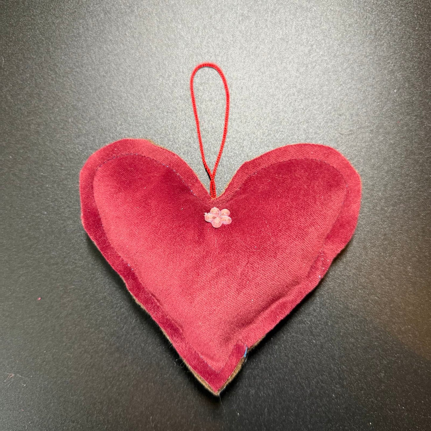 Red heart-shaped fabric ornament with a string on a gray background